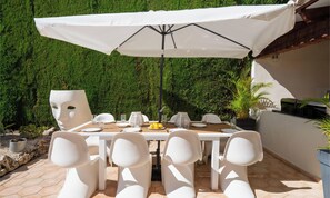 An outdoor dining area with a table set for four, surrounded by white chairs, under a large umbrella. - Villa Eliana • Artistic escape with family pool (Moraira)