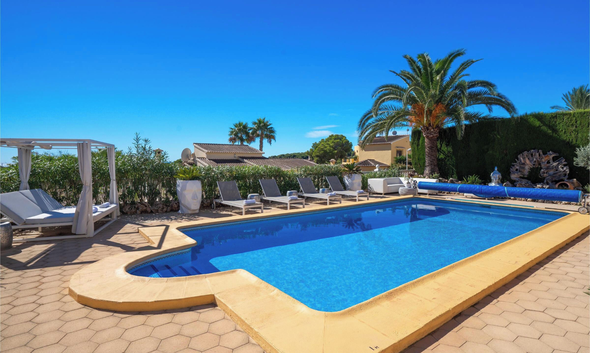 Una piscina rectangular con borde curvo, rodeada de sillones de descanso y una pérgola.