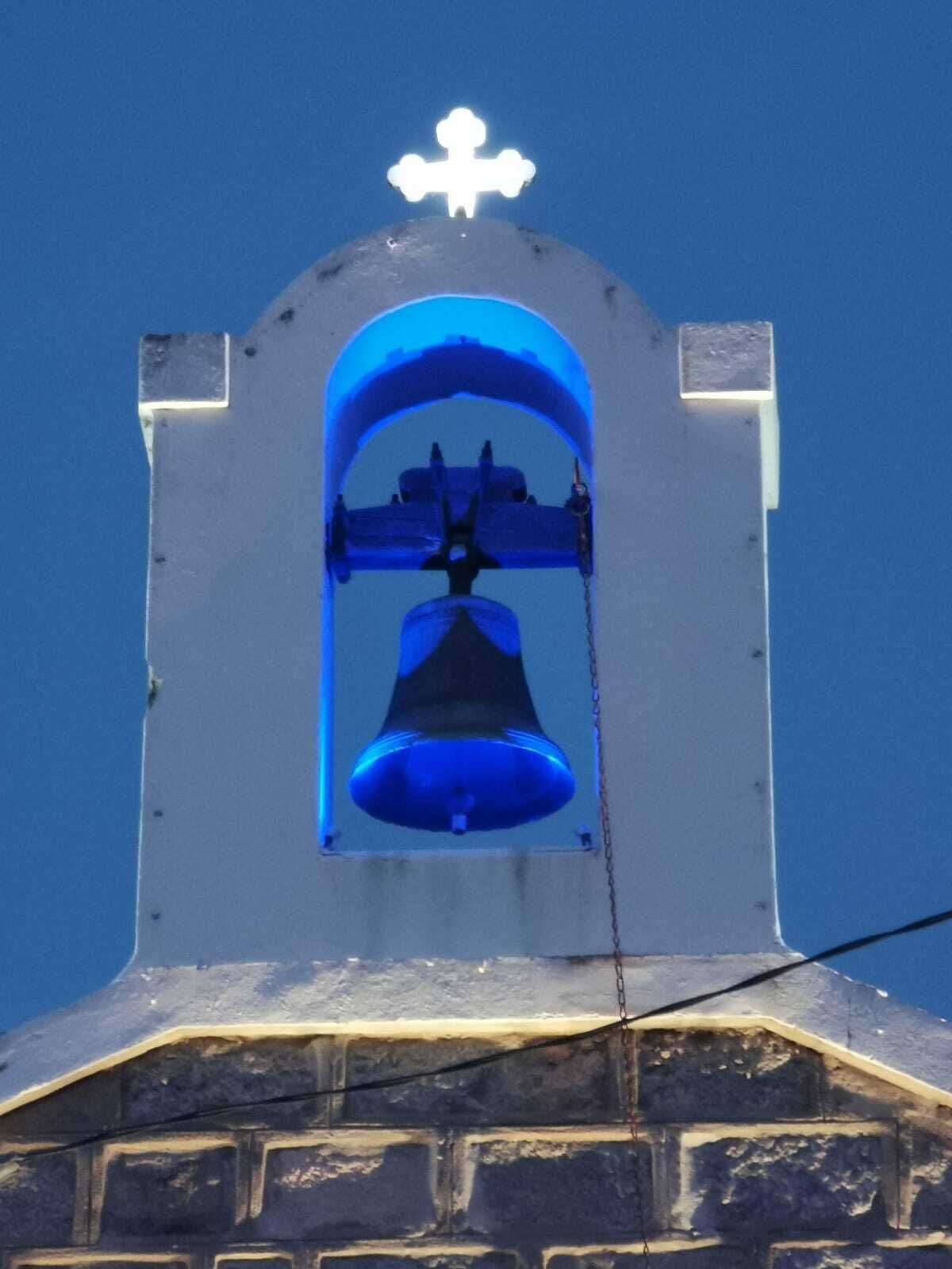 Ein Glockenturm mit einer Glocke darin, einem Kreuz an der Spitze und einem Backsteinfundament.