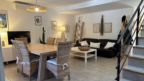 Ett modernt vardagsrum med en matplats, med ett träbord, flätade stolar, en svart soffa och en trappa.