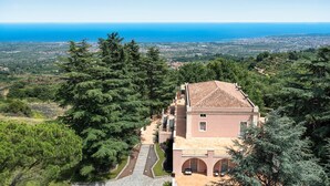 A coastal villa with a terracotta roof, surrounded by dense greenery and overlooking a coastal landscape. - Luxury pool villa between Taormina and Catania, Sicily (Mascali)