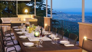 A dining table set for six with chairs, a lamp, and a view of a cityscape at dusk. - Luxury pool villa between Taormina and Catania, Sicily (Mascali)