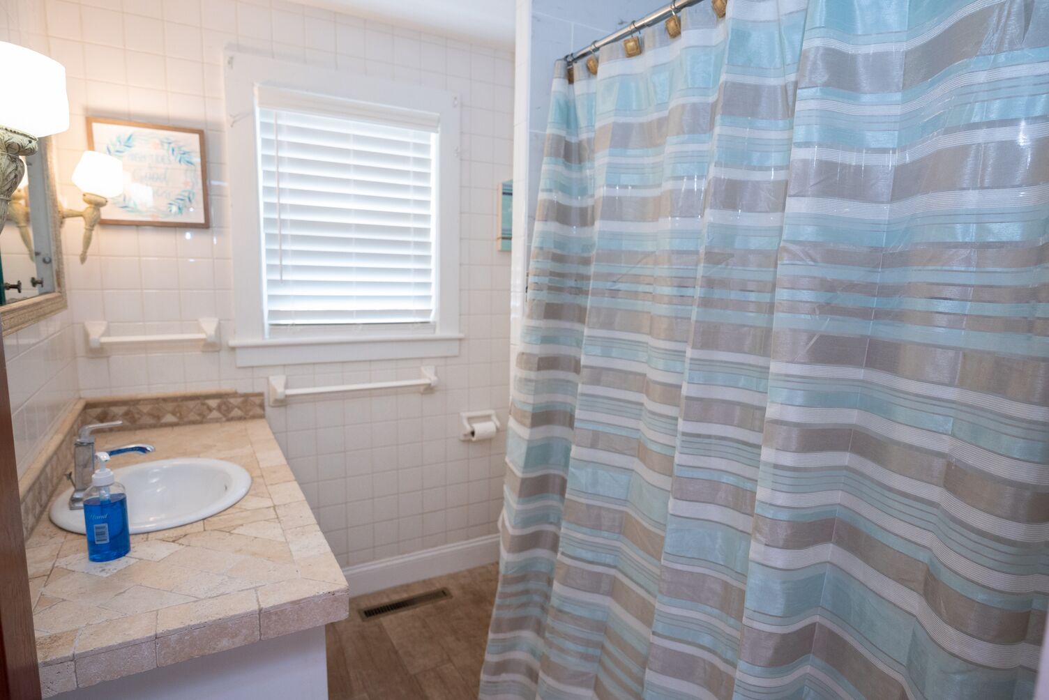 A bathroom with a white sink, a window with blinds, a shower curtain, and a towel rack.