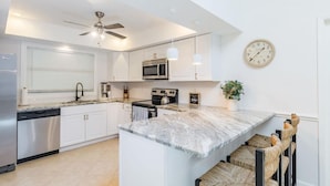 A modern kitchen with white cabinets, a marble countertop, a built-in microwave, and a ceiling fan. - Coastal Getaway minutes from Siesta Key, America’s #1 Beach (Sarasota)