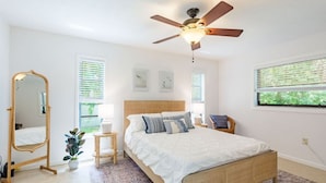 A bedroom with a bed, a ceiling fan, a mirror, a small table with a plant, and a window with blinds. - Coastal Getaway minutes from Siesta Key, America’s #1 Beach (Sarasota)