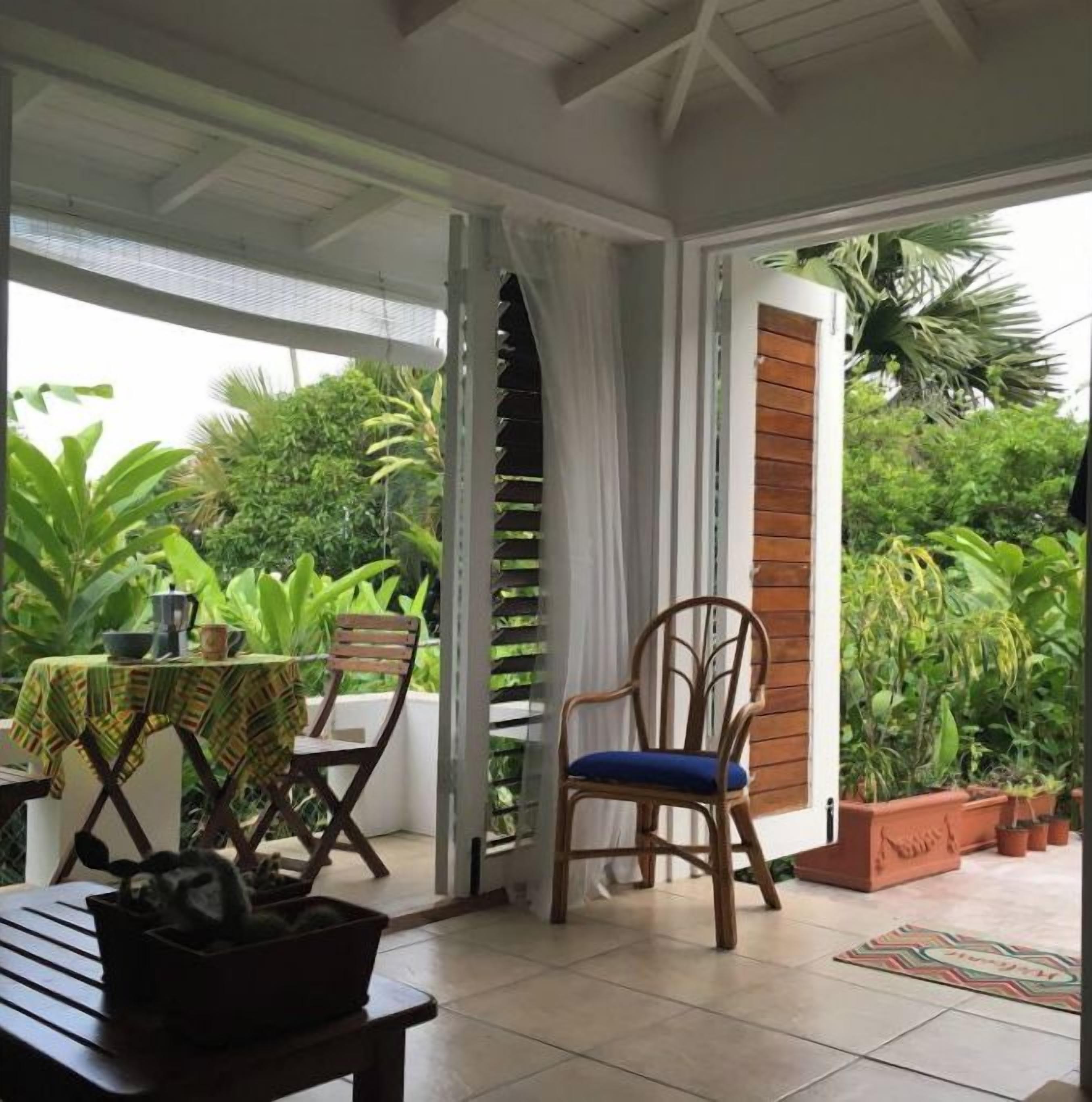 A covered patio with a table, chairs, and potted plants.
