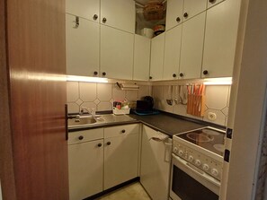 A compact kitchen with white cabinets, a stove, and a sink.