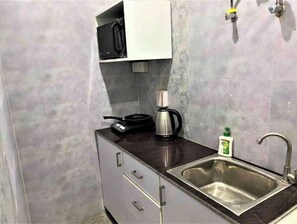 Compact kitchen area with a stainless steel sink, black countertop, and white cabinet.