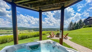 A hot tub under a wooden pergola with a view of a grassy landscape and a lake. - Lake Access, Dock, Hot Tub, Fire Pit , Free Golf + Pickle Ball (Swanton)