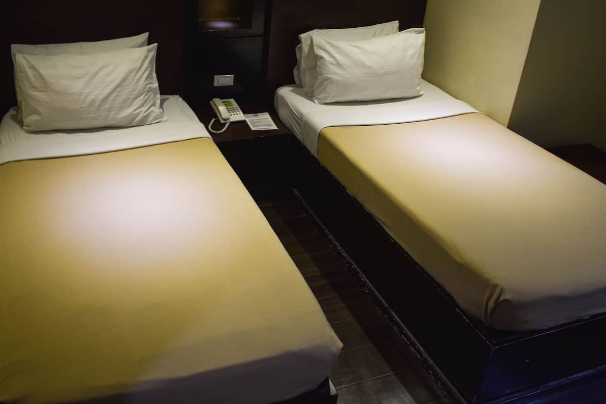 Two single beds with white linens, a bedside telephone, and a dark-colored nightstand.