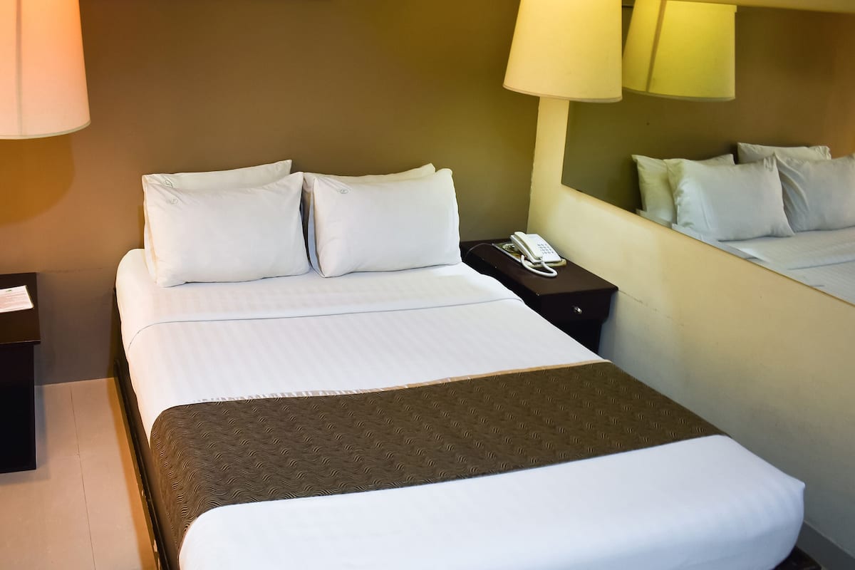 A hotel room with a bed, bedside lamps, a phone, and a mirror.