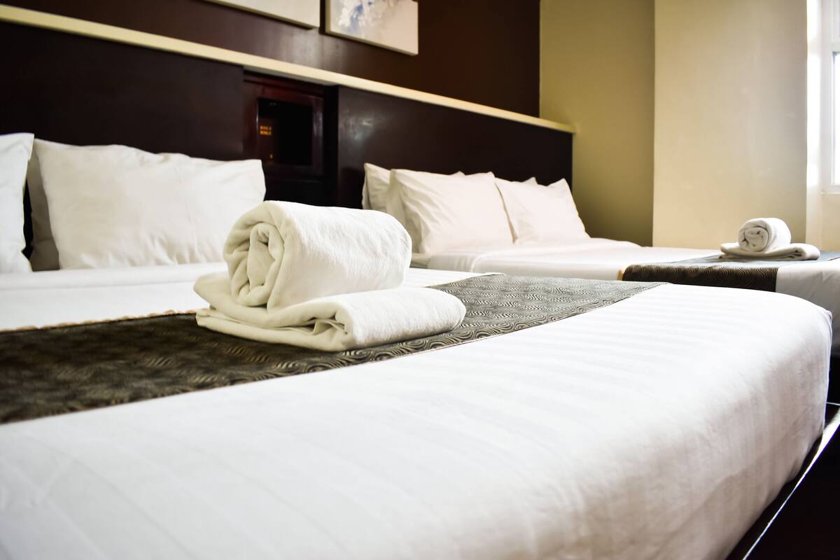 A hotel room with two beds, white linens, and a neatly folded towel on each bed.