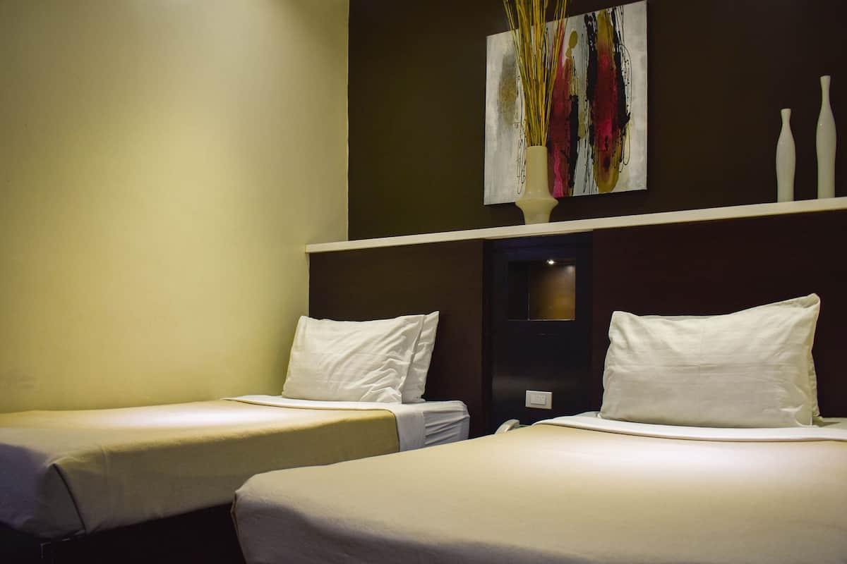 A hotel room with two single beds, a painting above the bed, and a shelf with vases.