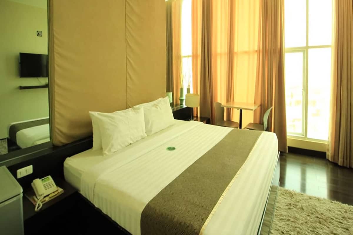 A hotel room with a bed, a desk, a chair, a telephone, and a window with curtains.