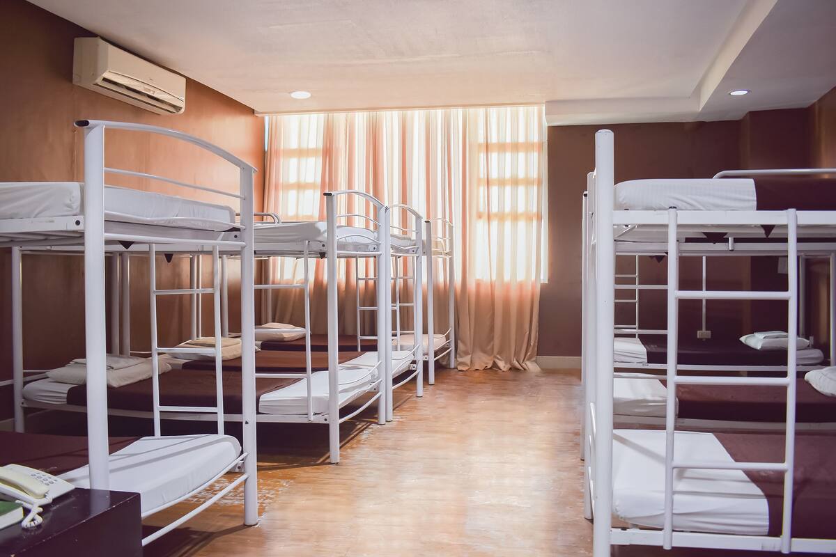 A room with bunk beds, a wooden floor, and a window with curtains.