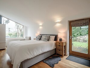 Une chambre à coucher avec un grand lit, des tables de chevet, une fenêtre et une vue sur l’extérieur.