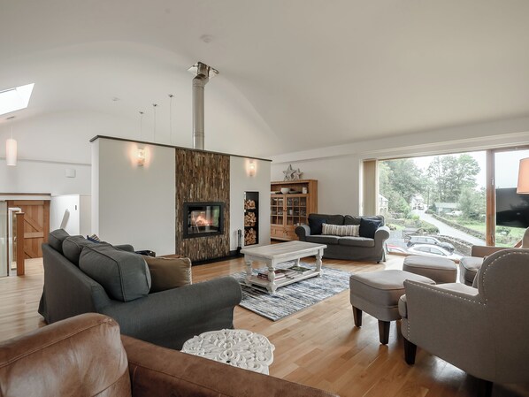 Un salon spacieux doté d’une cheminée, d’un plancher en bois et d’une grande fenêtre offrant une vue sur l’extérieur.
