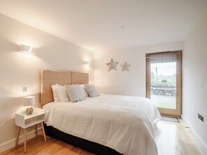 Ein Schlafzimmer mit Bett, Nachttisch, Lampe, Wandleuchten und Blick durch eine Tür.