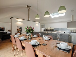 A modern dining area with a wooden table set for six, surrounded by chairs. A vase with flowers is placed on the table.