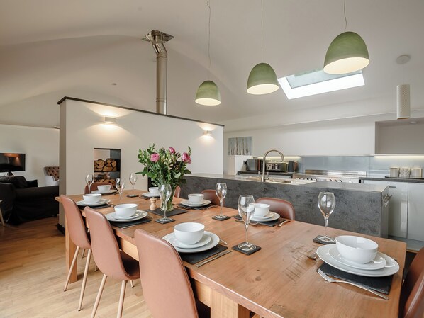 Un espace repas moderne avec une table en bois dressée pour six personnes, entourée de chaises. Un vase rempli de fleurs est posé sur la table.