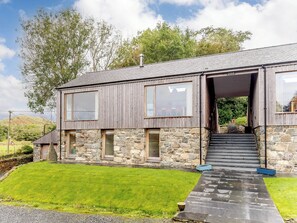 Une maison moderne à deux étages, dotée d’une façade en pierre et de grandes fenêtres.