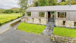 A modern house with a stone facade, large windows, and a gravel driveway. - This striking home is ideally located between the beach and the hills. (Arthog)