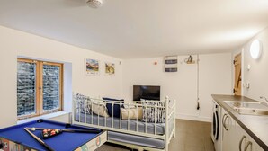 A room with a pool table, a crib, a television, and a washing machine. - This striking home is ideally located between the beach and the hills. (Arthog)