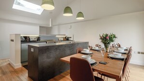 A modern kitchen with a central island, a dining area with a wooden table and chairs, and pendant lighting. - This striking home is ideally located between the beach and the hills. (Arthog)