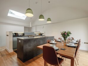 Une cuisine moderne dotée d’un îlot central, d’un coin repas avec une table et des chaises en bois, et d’un éclairage suspendu.
