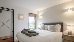 A bedroom with a bed, a nightstand, a lamp, a wall-mounted light, a window with a view, and a door. - This striking home is ideally located between the beach and the hills. (Arthog)