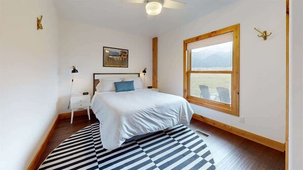 A bedroom with a bed, a nightstand, a lamp, a window with a view, and a ceiling fan.