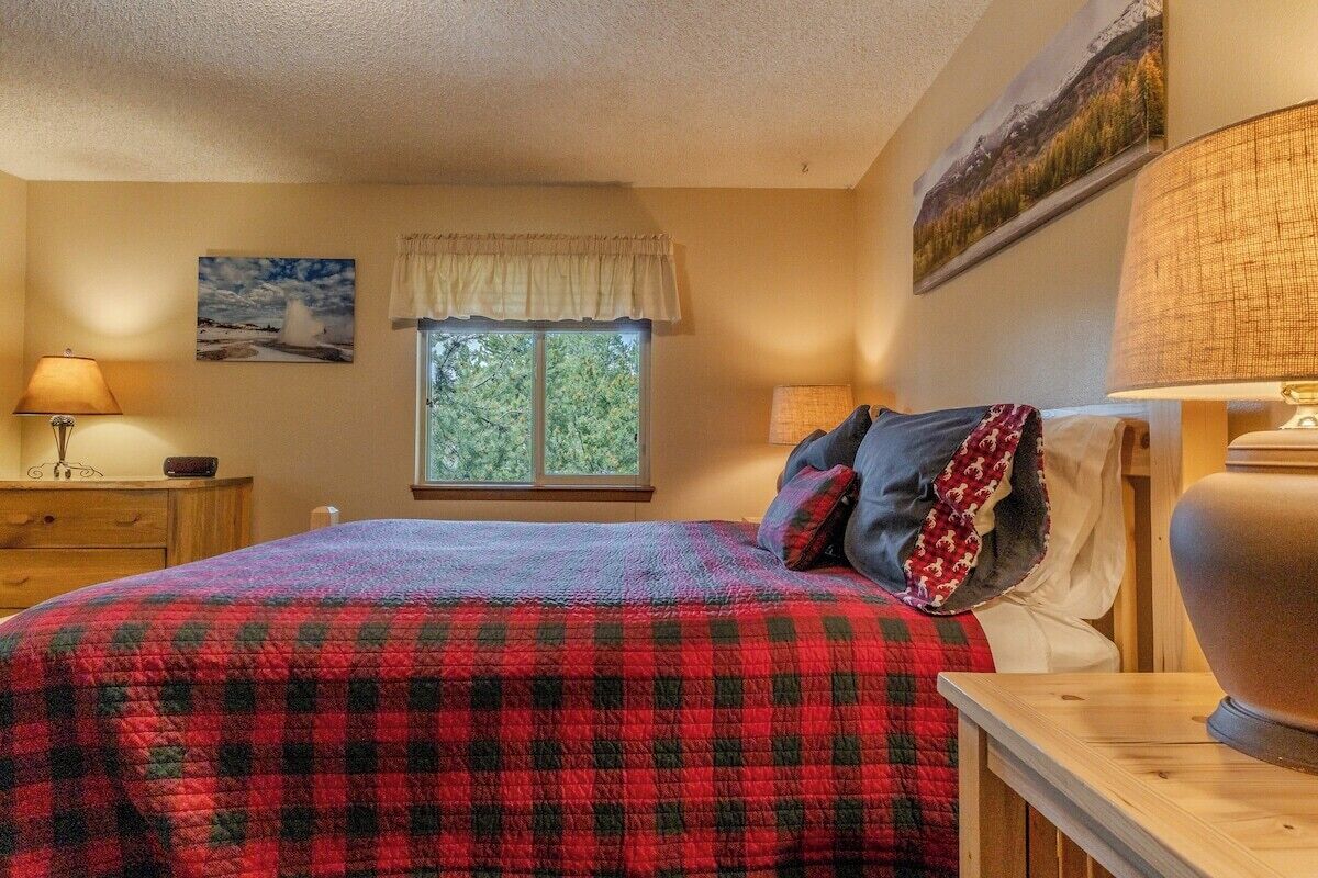 A bedroom with a bed, a window with a view, a lamp, and a painting on the wall.
