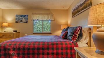 A bedroom with a bed, a window with a view, a lamp, and a painting on the wall.