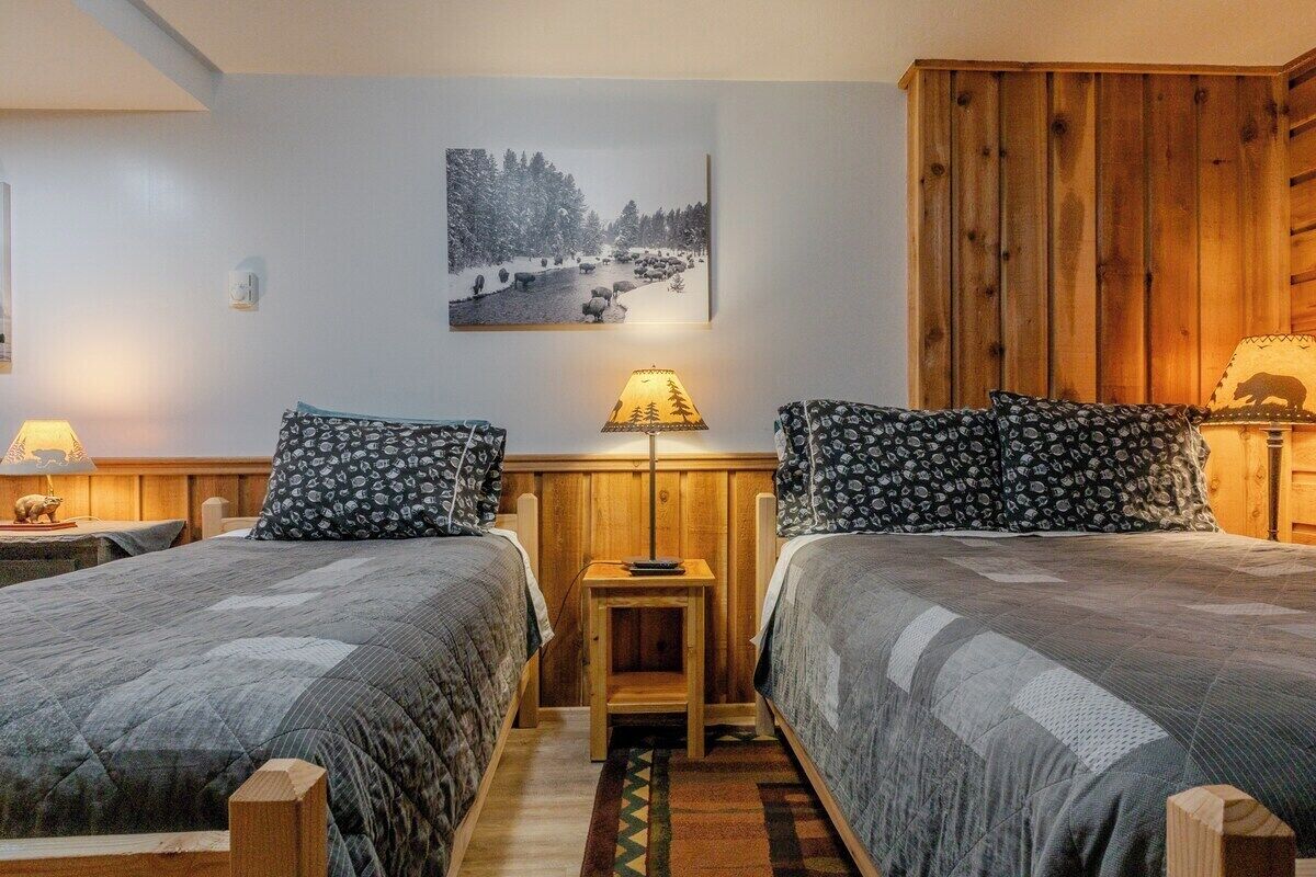 Een kamer met twee bedden, een houten kast, een lamp en een schilderij aan de muur.