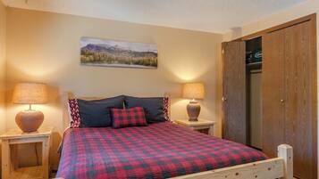 A bedroom with a bed, two bedside lamps, a wooden headboard, a door, and a wall-mounted picture.