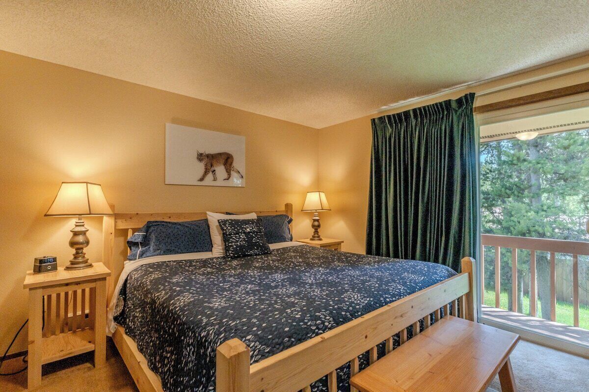 Een slaapkamer met een bed, twee nachtkastjes, een bankje, een raam met gordijnen en een aan de muur hangend schilderij.