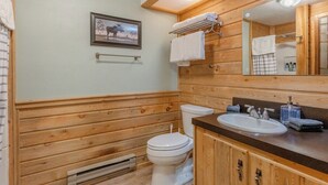 A wooden-paneled bathroom with a white toilet, a sink with a mirror, and a towel rack. - The Trailhead Townhouse (West Yellowstone)