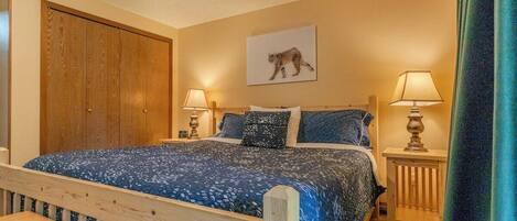 A bedroom with a wooden bed, two bedside lamps, a wooden nightstand, and a large wooden wardrobe.