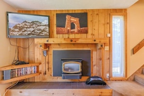 A room with a fireplace, wooden shelves with books, a television mounted on the wall, and a window.
