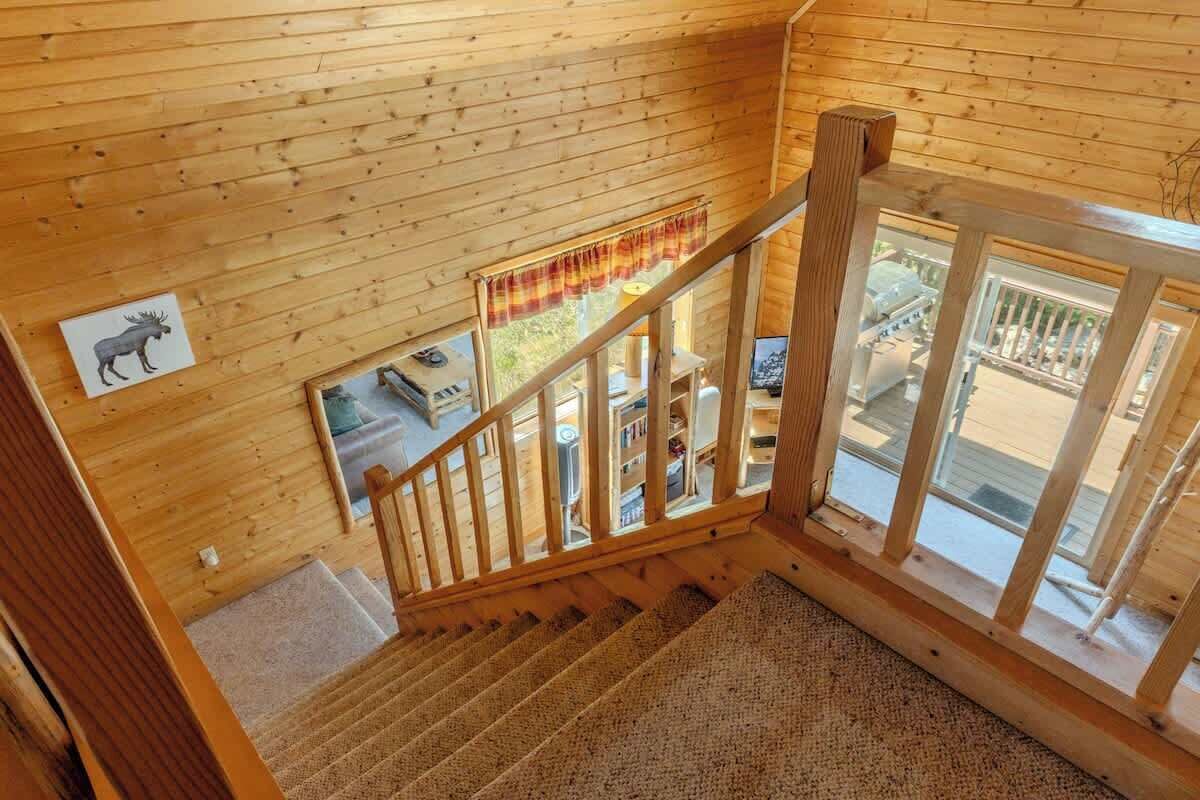 A wooden interior with a staircase, a window with a view, and a moose sign on the wall.