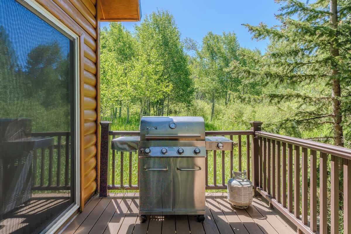 A barbecue grill on a wooden deck with a glass door and a view of a forest.