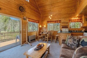 A wooden cabin with a dining area, kitchen, and a sofa with a view of the outdoors. - The Aspen House (West Yellowstone)