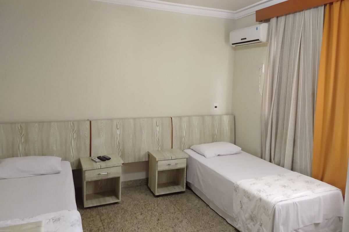 Une chambre d’hôtel avec deux lits simples, une tête de lit en bois, une table de chevet avec un téléphone et un appareil de climatisation.