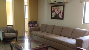 Una sala de estar con un sofá color beige, una mesa de centro de vidrio, una silla roja y un cuadro en la pared.