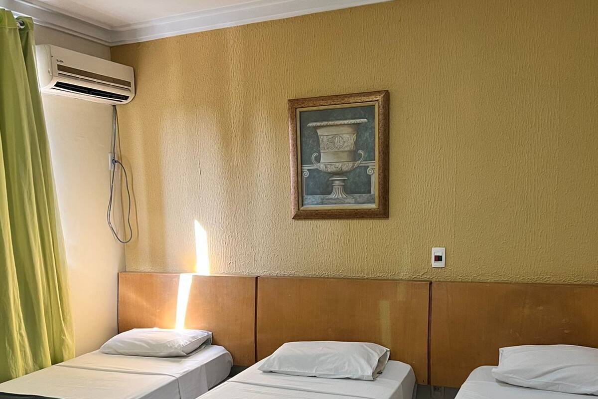 Une chambre d’hôtel avec deux lits simples, une tête de lit en bois, un tableau encadré au mur et un appareil de climatisation.