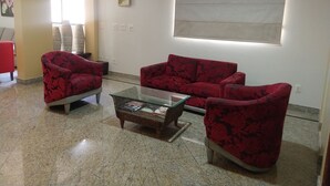 Un salón con un sofá rojo estampado floral, una mesa de centro de vidrio y un sillón con estampado.