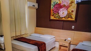 Habitación de hotel con dos camas, cabecero de madera, un cuadro de flores, una mesita de noche de madera y una ventana con cortinas.