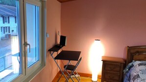 Een slaapkamer met een houten plafond, een bureau met stoel, een nachtkastje en een bed met bloemenbedekking.