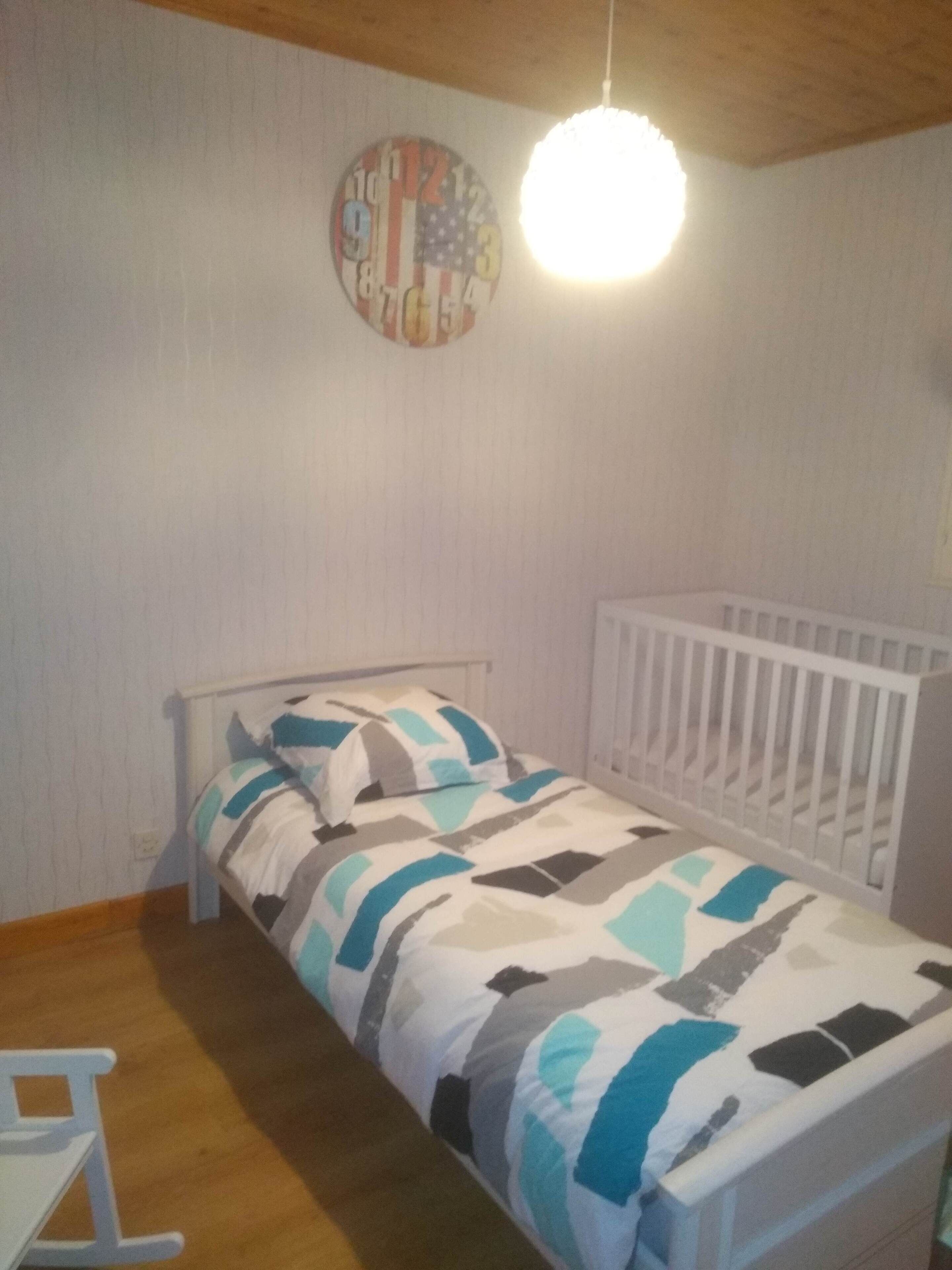 Un dormitorio pequeño y ordenado con una cama individual, una cuna y un reloj de pared.