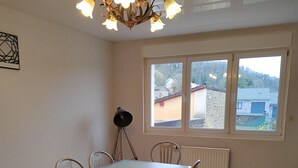 Een eethoek met een tafel, stoelen, een radiator, een raam met uitzicht en een plafondlamp.